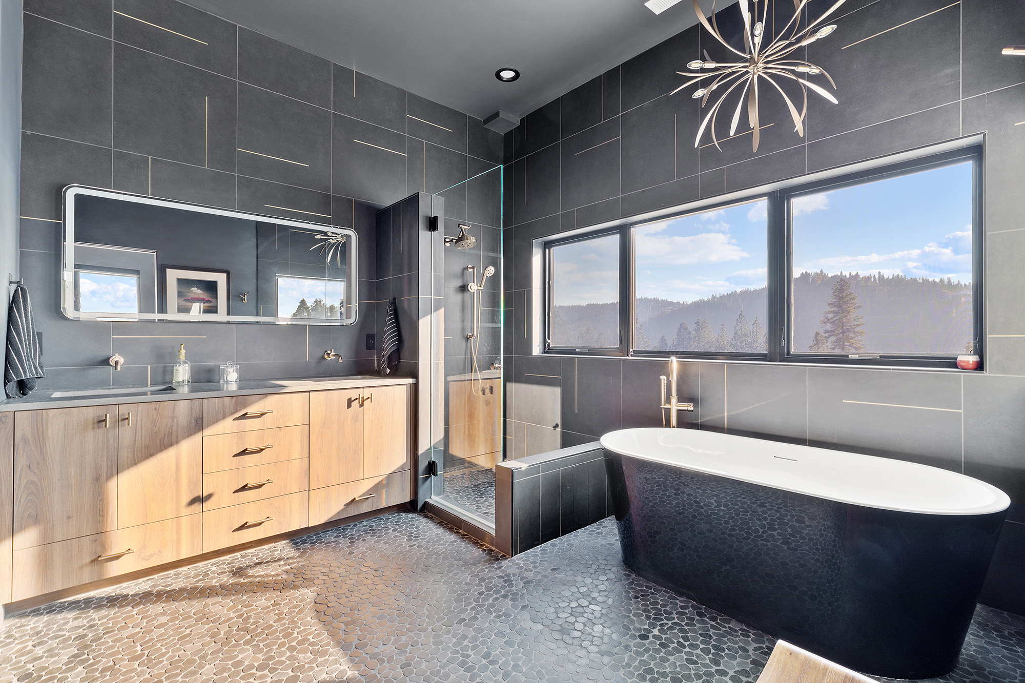 Primary bathroom at Fernan Hill Residence in Coeur d’Alene with freestanding tub, dual vanity, and natural stone finishes designed by Fusion Architecture