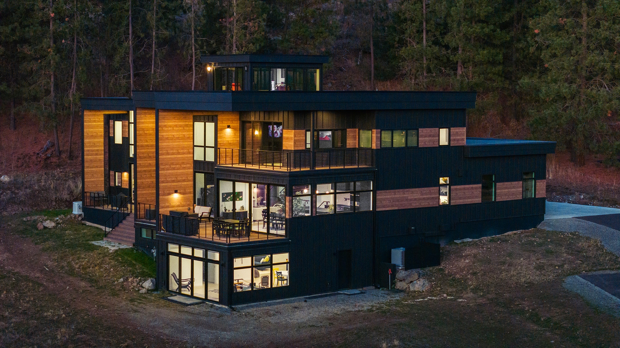 Fernan Hill Residence in Coeur d’Alene, Idaho at dusk with warm interior lighting glowing through expansive glass walls, highlighting modern architectural lines